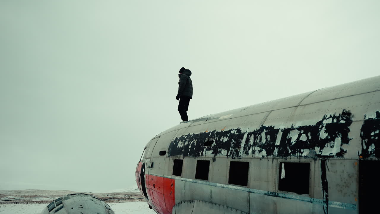 Gradual Dolly in of Man Dressed for Winter Standing Atop Wreckage of an Old Abandoned Plane, Iceland