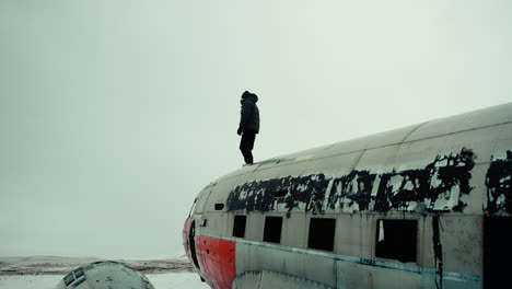 gradual dolly in of man dressed for winter standing atop wreckage of an old abandoned plane, iceland