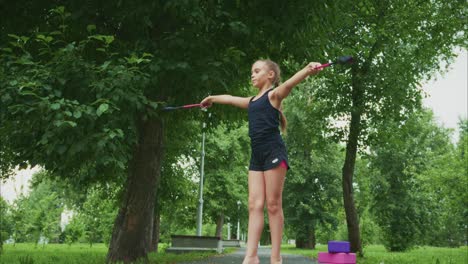 a young girl demonstrates impressive balance and poise while practicing rhythmic gymnastics in a serene park setting, showcasing her talent with rhythmic apparatus