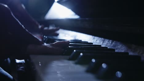 close up of hands playing piano in low light