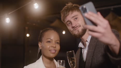 man and woman toasting with champagne glasses while taking a selfie video at new year's eve party 1