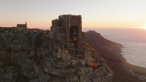 Rutsche-Und-Schwenk-Der-Oberen-Seilbahnstation-Auf-Dem-Tafelberg-Bei-Sonnenuntergang.-Erstaunliches-Filmmaterial-Zum-Bauen-Auf-Einem-Hohen-Felsen-über-Dem-Tal-Und-Der-Küste.-Kapstadt,-Süd-Afrika