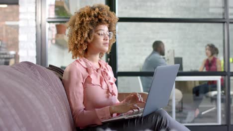 Thoughtful-biracial-casual-businesswoman-using-laptop-on-couch-in-office,-copy-space,-slow-motion