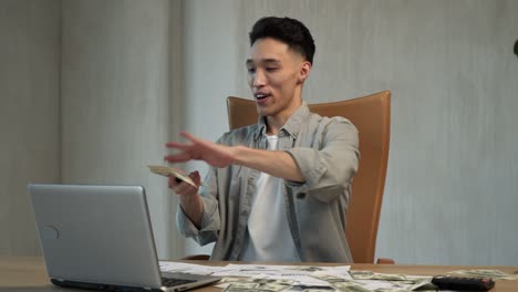 happy asian businessman throws dollar bills on table