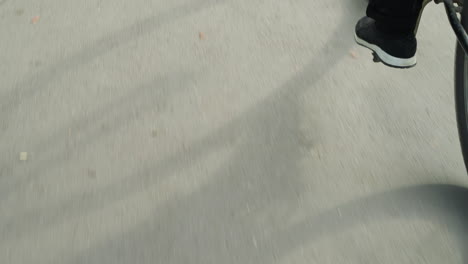 close-up of someone pedaling bicycle slowly, with detailed view of sneakers and black trousers, casting a distinct shadow of the bike and rider on the sunlit pavement