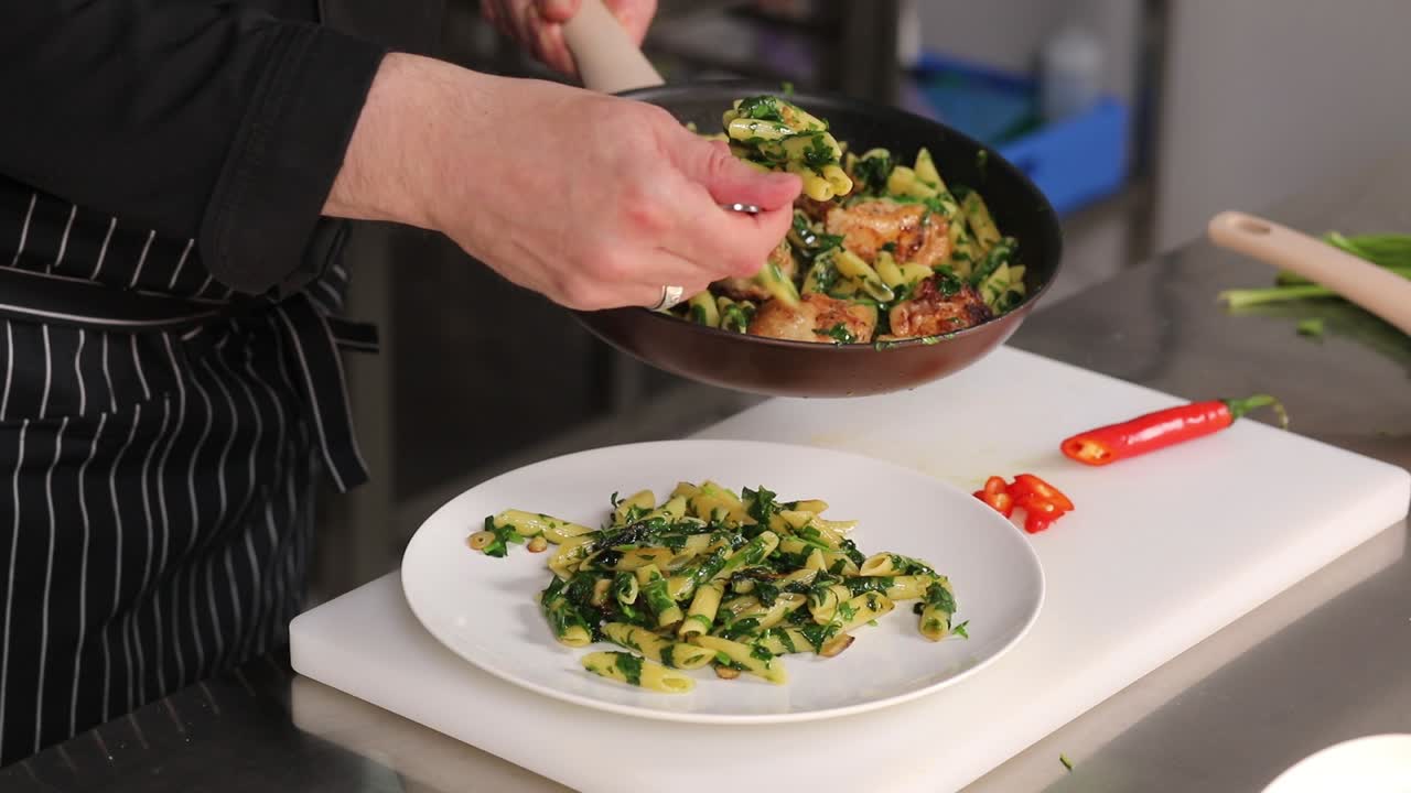 Chef preparing a dish of penne pasta with spinach and chicken
