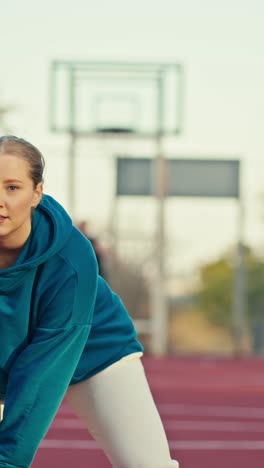 woman in teal hoodie and white pants working out on a track
