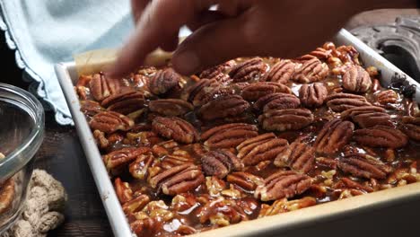 baking delicious caramel pecan brownies. using my hands to place whole pecans into the caramel topping. freshly baked gooey chocolate brownies with sweet caramel and nutty pecans.