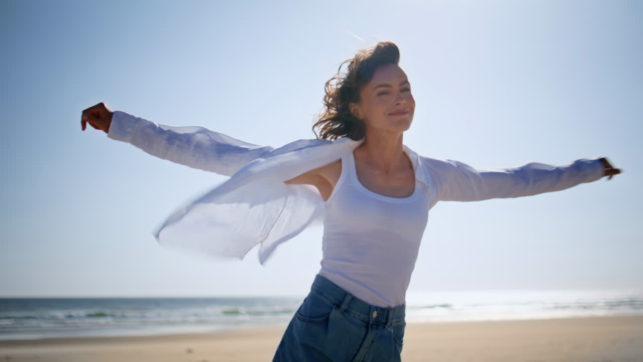 Woman spinning sunny sea shore raising hands to blue sky closeup