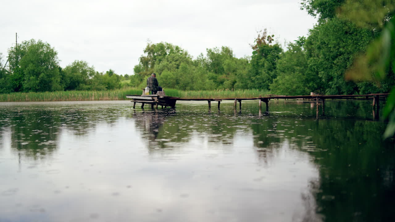 Old man is fishing on the old pier. Calm leisure of grandfather at nature