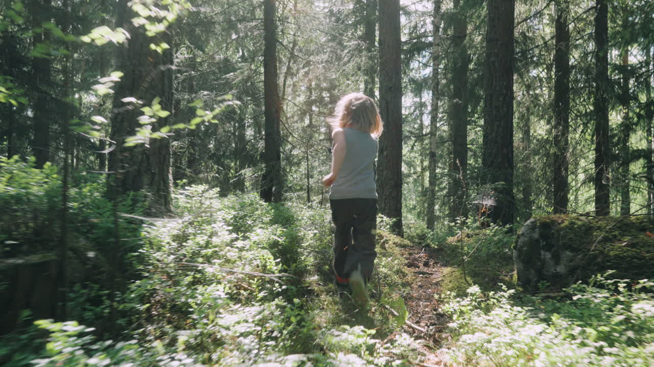 Wild child runs through remote woods as sun flits through trees, rear tracking
