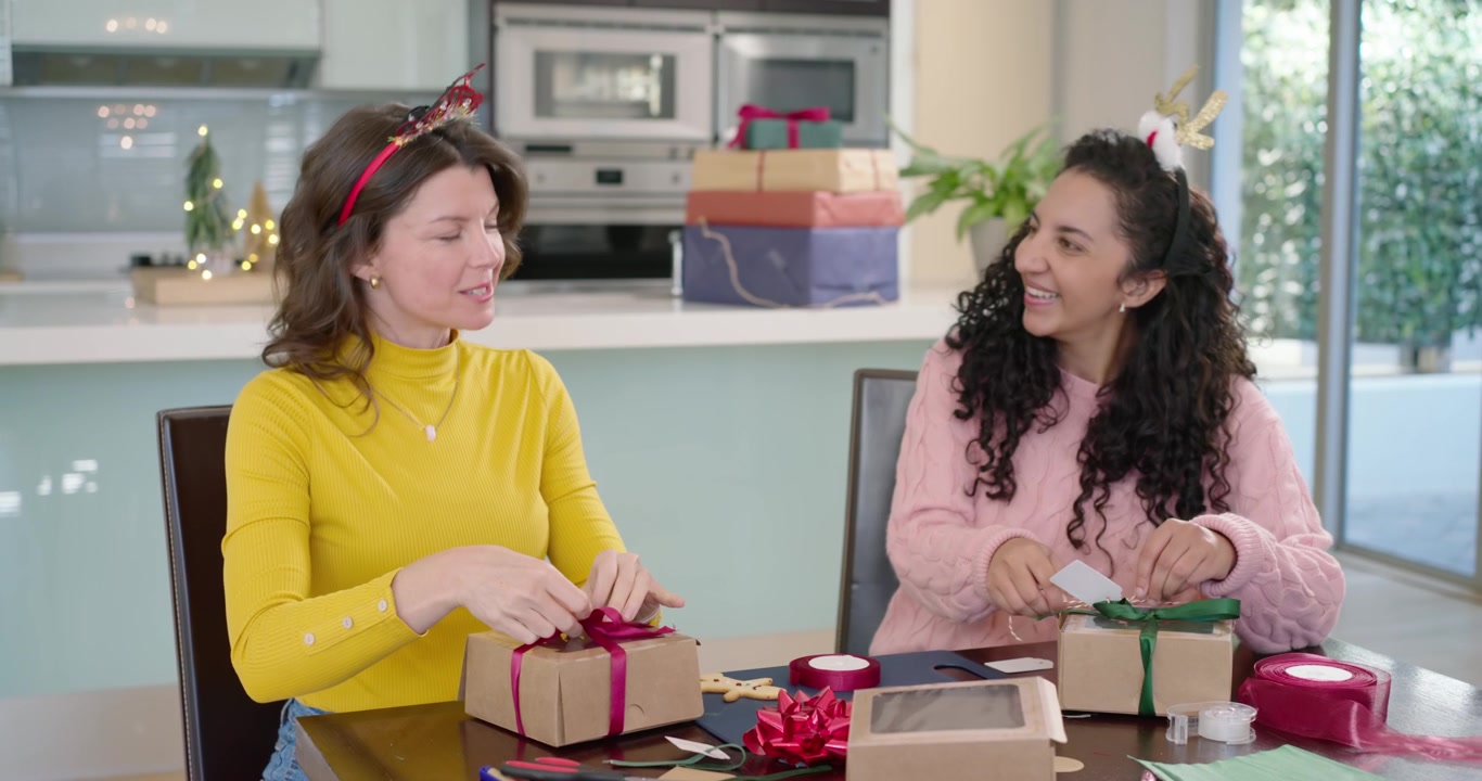 Amigas diversas embrulhando presentes de papel kraft na mesa da cozinha para as festas, amarrando fitas.
