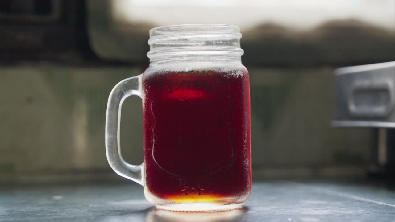 A closeup footage of pouring an ice cube into a glass of a iced tea, with blurred background