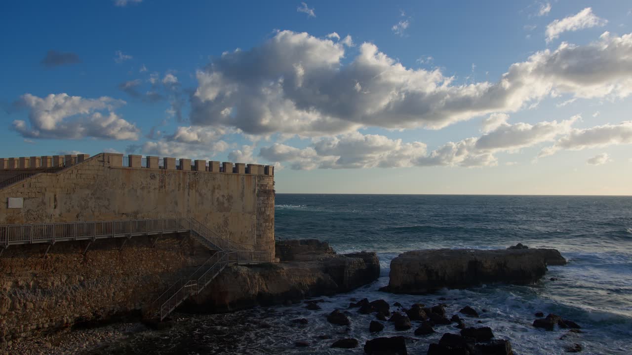 fotografía estática de una gran pared con el océano y las olas golpeando las rocas durante la hora dorada en siracusa, sicilia (sicilia, italia)
