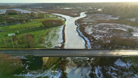 coche conduciendo sobre un puente sobre un río congelado durante el amanecer en letonia