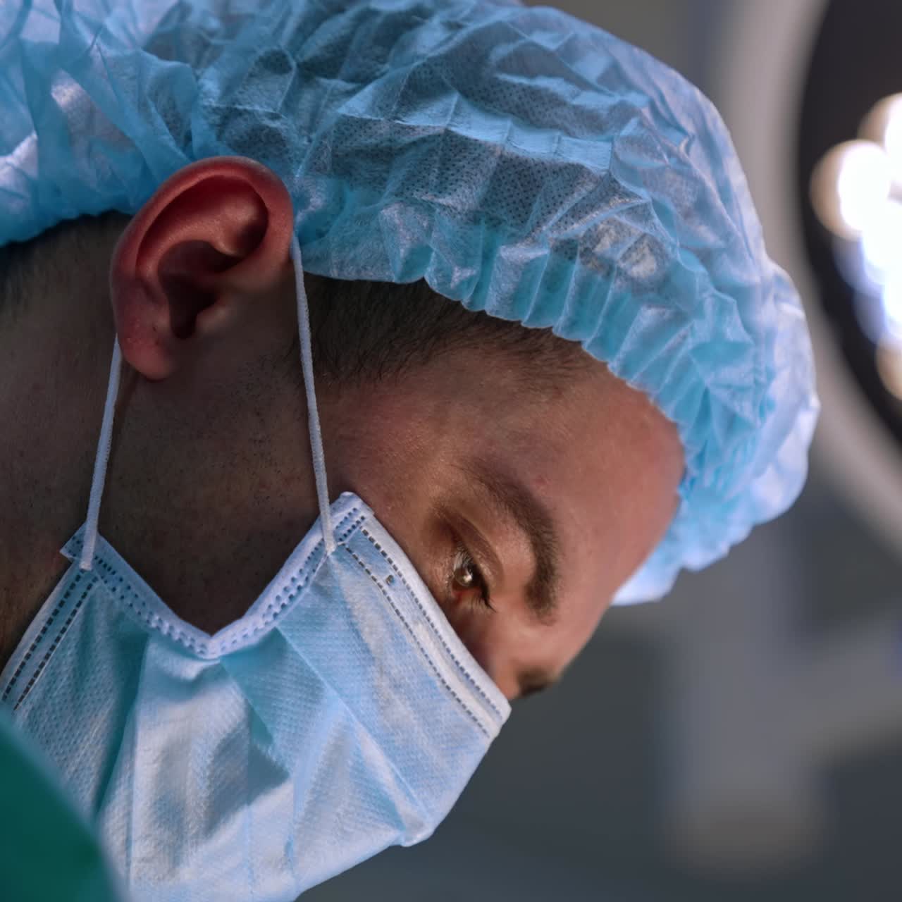 Face of a male doctor in cap and mask looking down. Side view portrait of a surgeon at operation. Close up