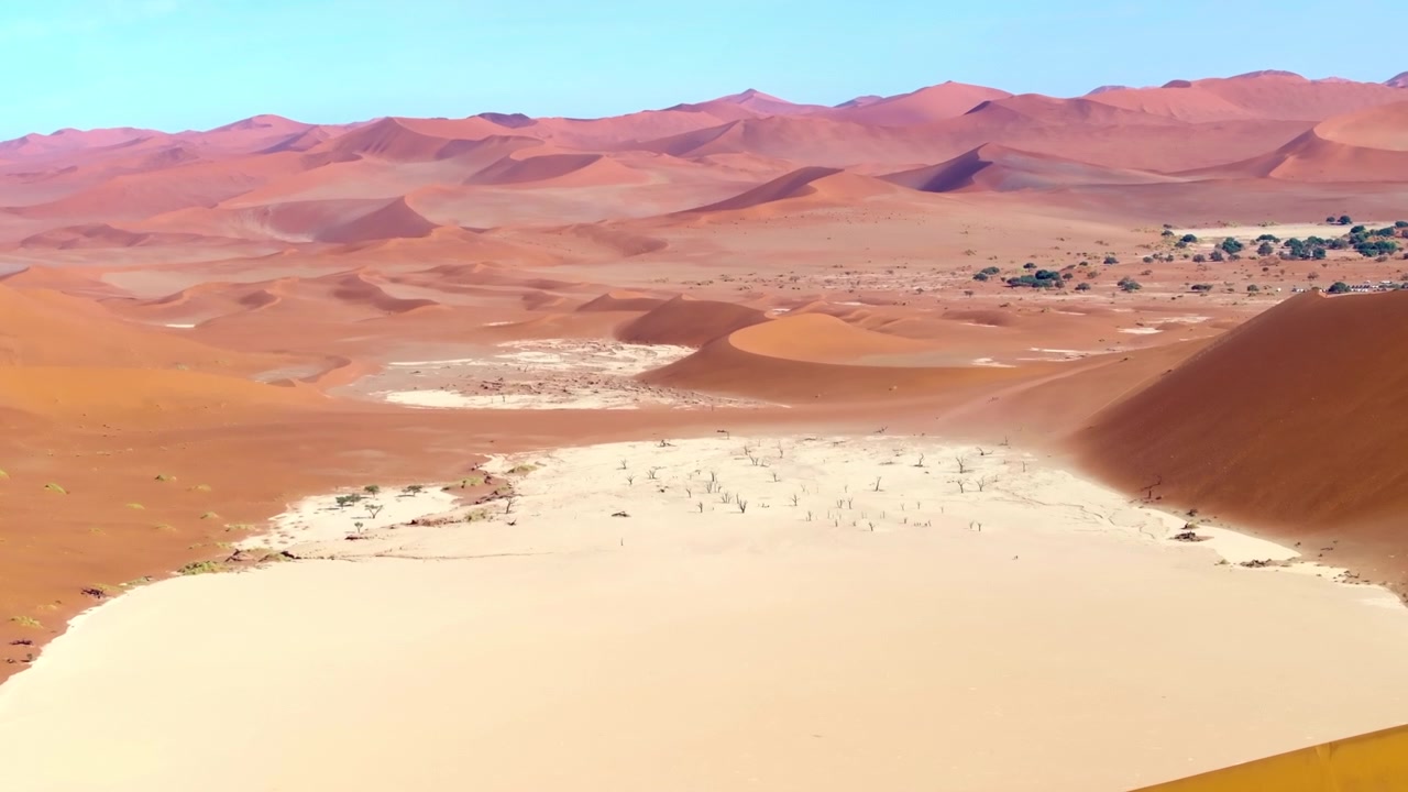 Vista de drone da planície de argila branca de Deadvlei pontilhada com antigas árvores de espinho de camelo mortas entre dunas vermelhas. Imponentes dunas vermelhas brilham sobre as planícies de argila pálida.