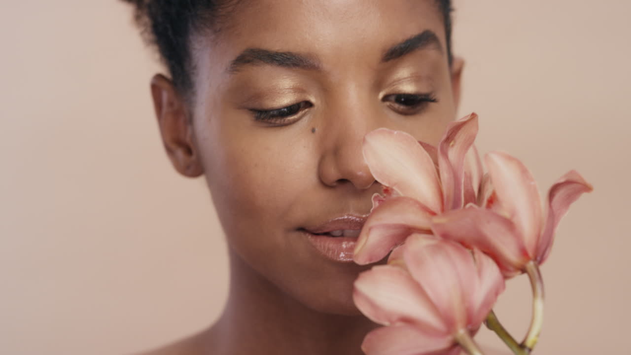 ritratto di bellezza bella donna afroamericana che posa giocosamente con un fiore di orchidea toccando una pelle sana che gode di una dolce fragranza di essenza naturale concetto di cura della pelle