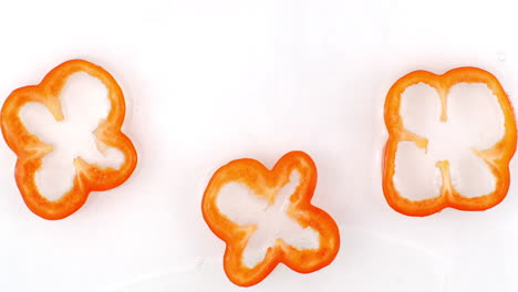 Water-splashes-in-slow-motion.-Top-view:-three-slices-of-red-sweet-pepper-washed-with-water-on-a-white-background