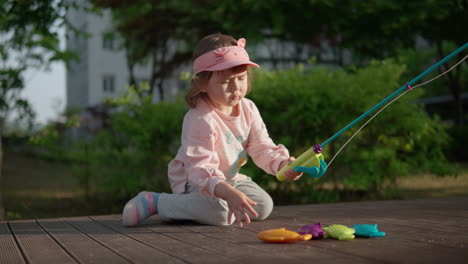 playful korean-ukrainian toddler playing with fishing toys on the ground at the park