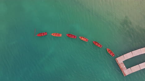 overhead drone top shot of red boats in curved formation on bright turquoise dolomites lake. lago di braies