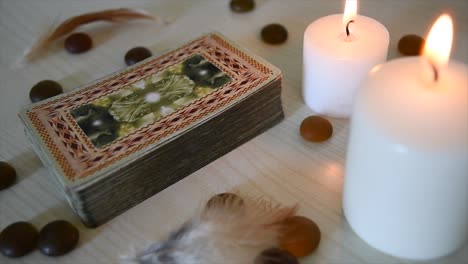 fondo con baraja de cartas místicas cerca de velas con llamas parpadeantes, piedras y plumas