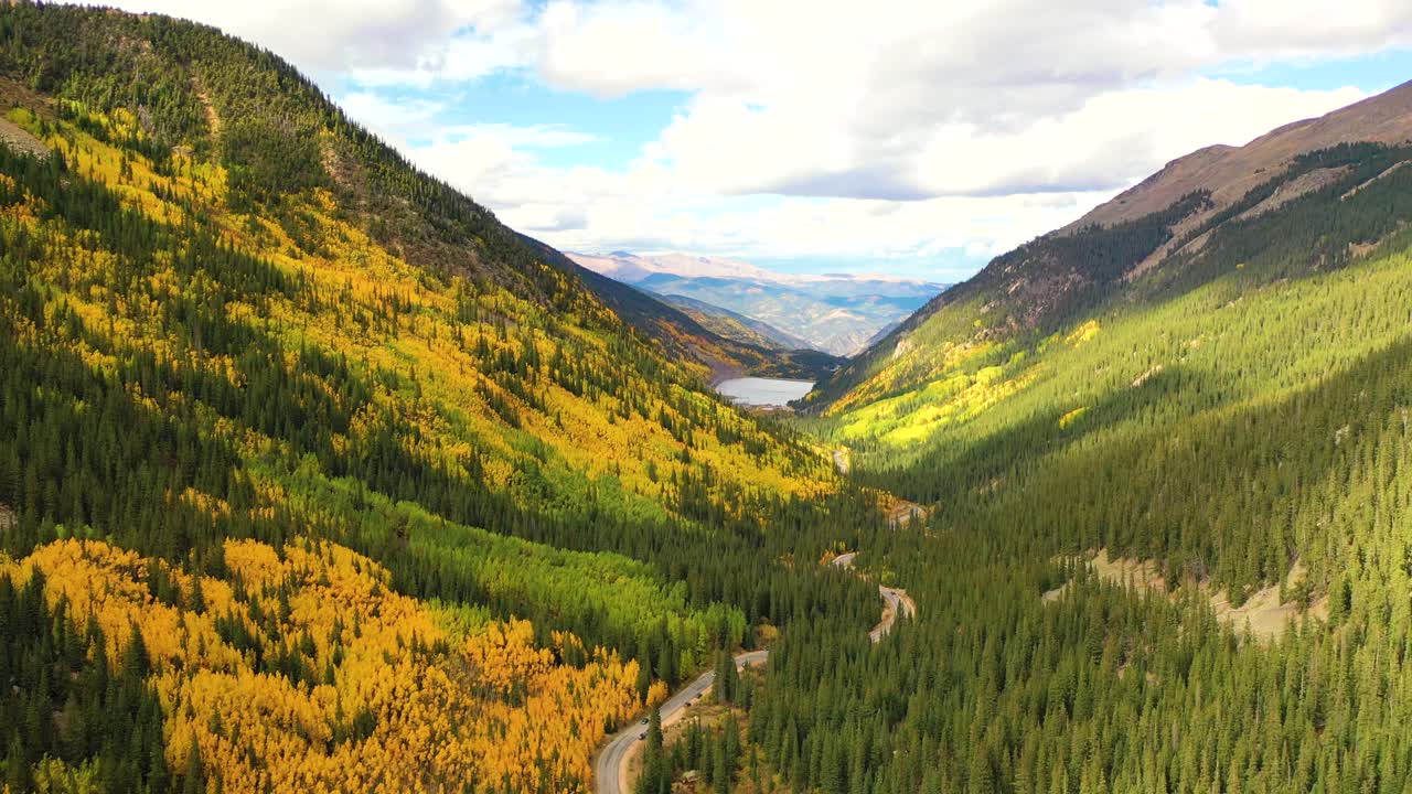 The Dolomites of Italy glow under autumn sunlight as golden forests climb steep limestone peaks and narrow roads curve through high alpine valleys