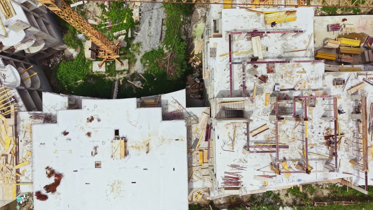 Una obra de construcción muestra un edificio inacabado con materiales esparcidos por la azotea en un entorno urbano durante el día.