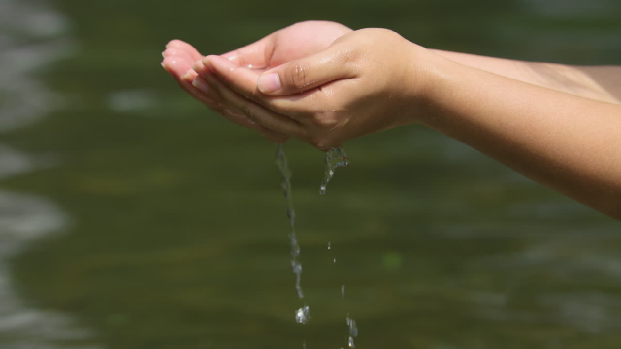 깨끗한 강에서 두 손으로 물을 퍼내는 여성