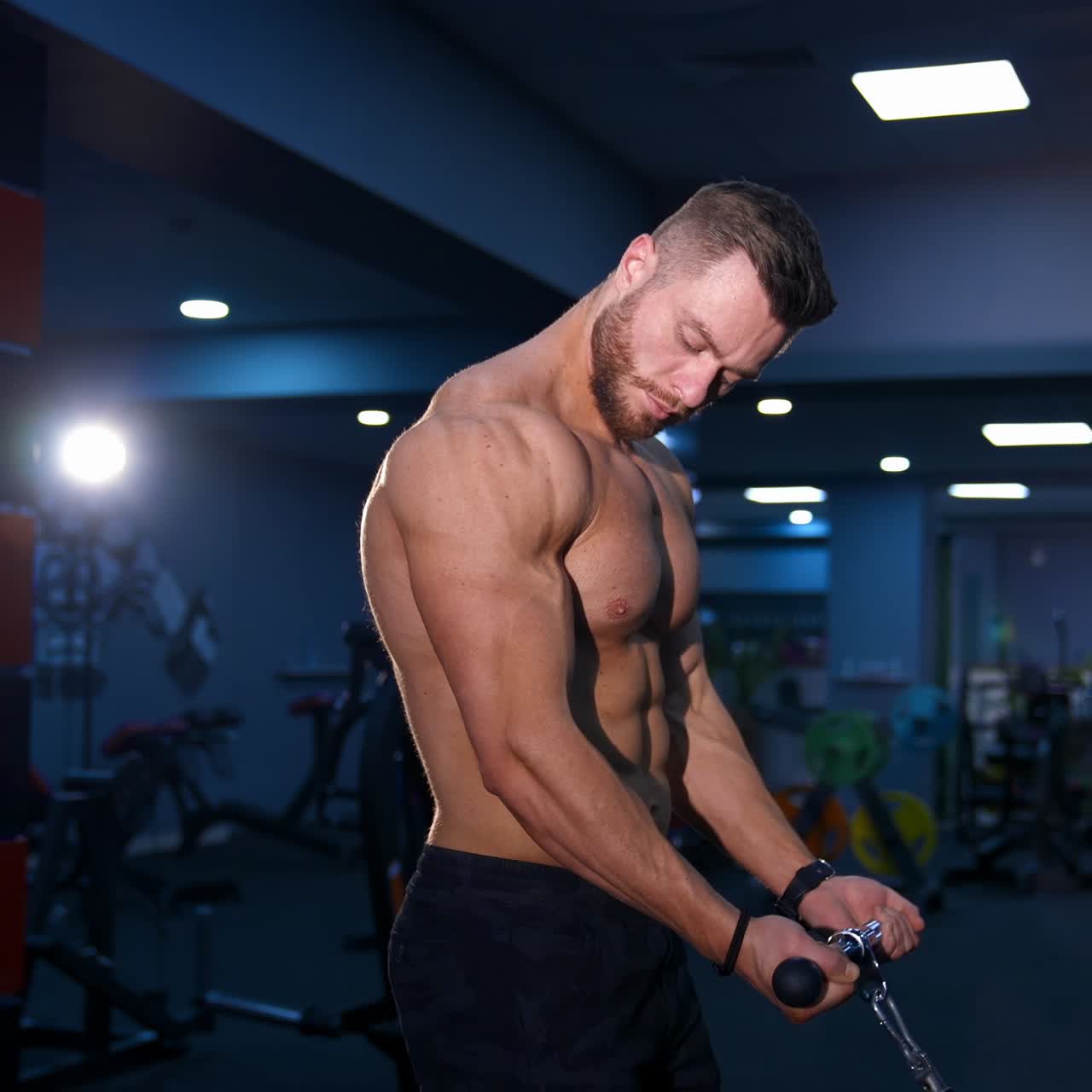 Giovane bodybuilder forte e attraente si allena su attrezzature sportive. Addominali scolpiti. Sfondo di palestra moderna. Video ripreso di lato.