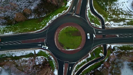 Aceleración-Aérea-Disparada-Por-Encima-Del-Tráfico-En-Una-Rotonda-Nevada,-Día-Nublado-De-Invierno