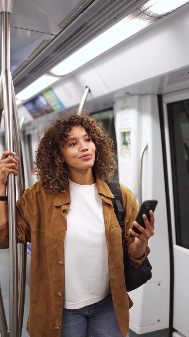 Young Woman with Curly Hair Using Phone on Subway Train