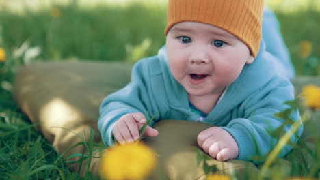 smiling toddler in warm clothes and cap enjoys staying outside. adorable little boy resting on the mattress in nature. close up.