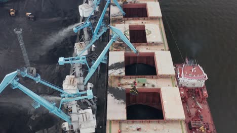 aerial drone close up view of coal transshipment to cargo ship with large cranes