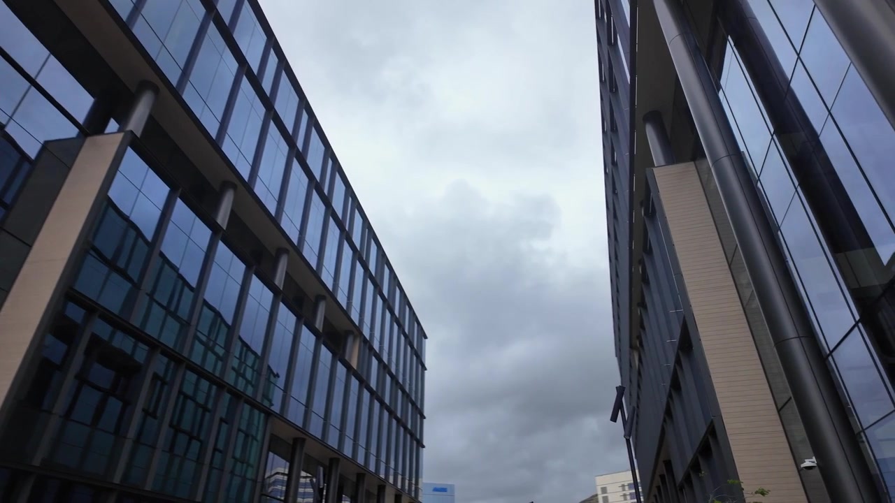 Toma en primera persona caminando que revela la fachada de cristal contemporánea de un edificio de investigación de laboratorio médico en el sur de San Francisco, California, bajo un cielo nublado y cubierto.