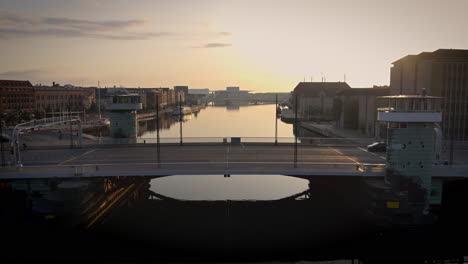 Drone-video-from-Copenhagen-harbour,-flying-slowly-backwards-from-a-bridge-over-the-canal,-revealing-a-beautiful-sunrise-and-the-city