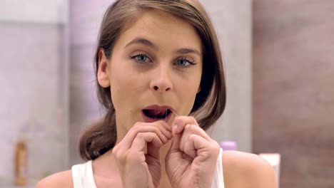 woman with dental floss cleaning her teeth in bathroom