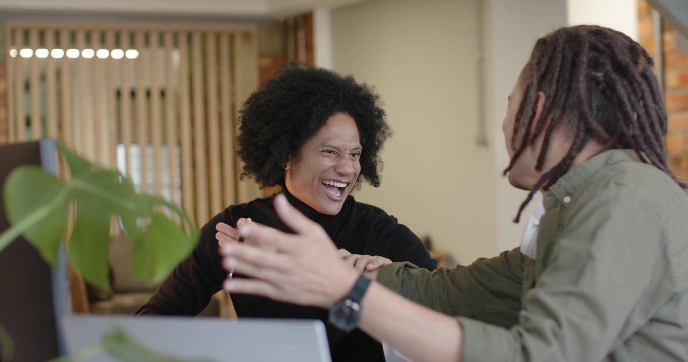 Diverse coworkers gesturing playfully and laughing after laptop prompt at office meeting, pens