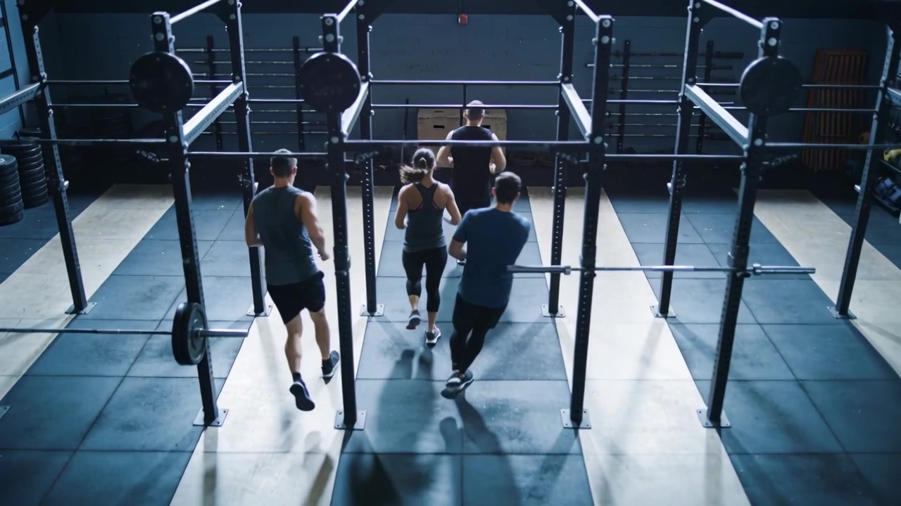 Running quartet wearing gym clothes starting interval run at gym, jogging past rig posts and plates