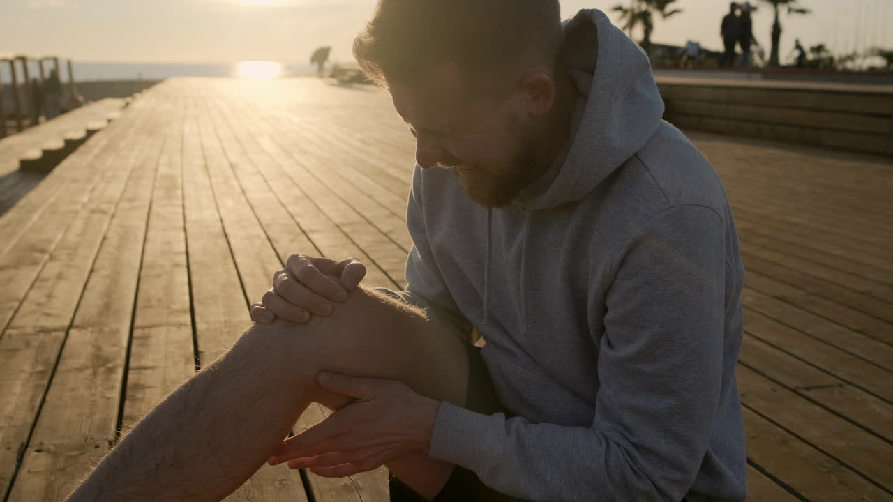 Man with a knee injury on a pier at sunset
