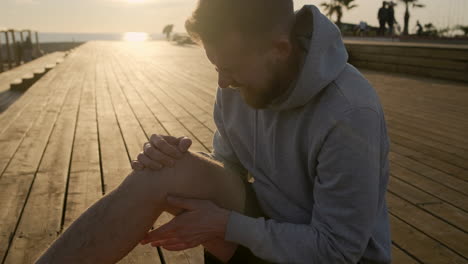 man with a knee injury on a pier at sunset