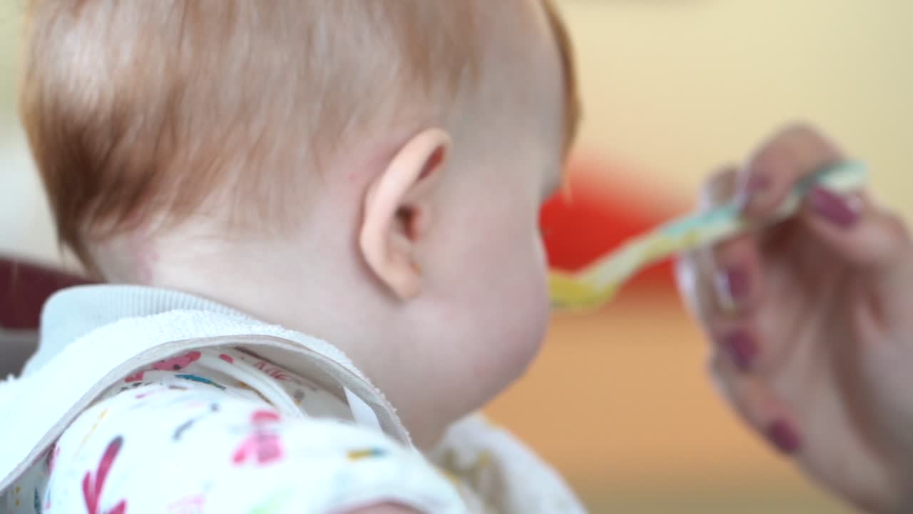 어머니의 손이 음식에서 머리를 돌리기로 결정한 아기에게 숟가락으로 먹이를 주려고 시도합니다.