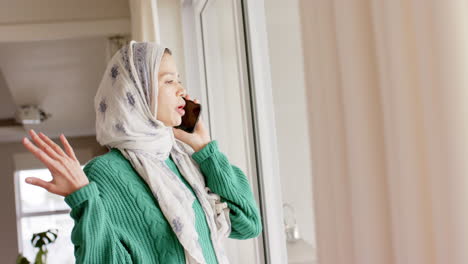 mujer biracial en hijab usando teléfono inteligente en casa con espacio de copia, cámara lenta
