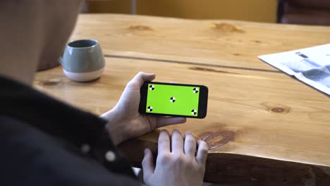 person holding smartphone with green screen on wooden table