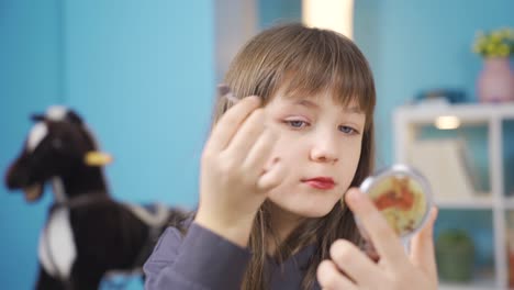 una niña divertida y alegre se maquilla a sí misma.