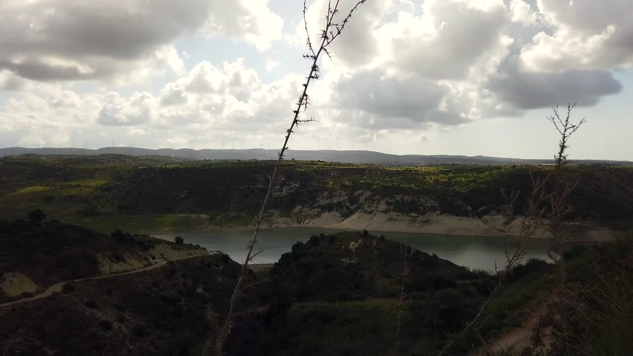 Cloudy spring day at Paphos Water Dam in Cyprus, low water levels visible. People with cars and camping gear at the water’s edge. A calm yet concerning scene of nature, leisure, and drought.