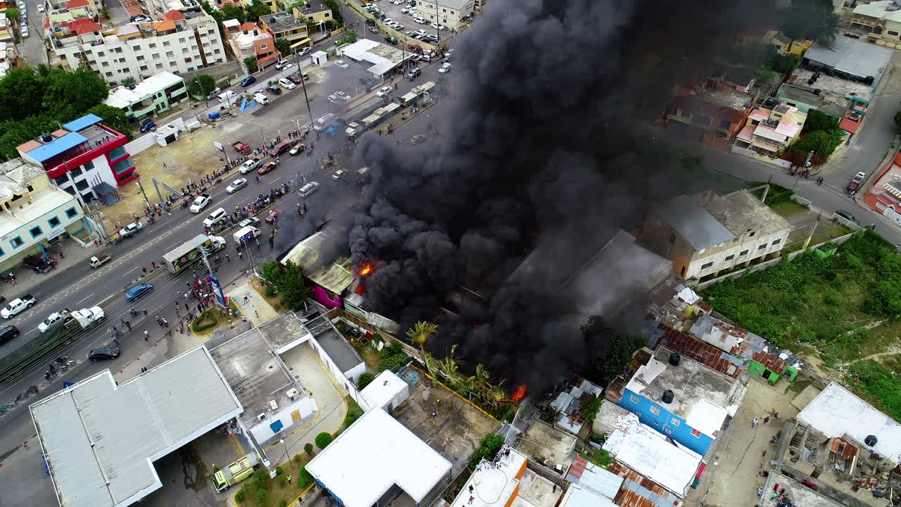 Aerial view around a building on fire, dark smoke rising from warehouse ruins, cloudy day, arson in San Juan, Puerto Rico, USA - High angle, orbit, drone shot