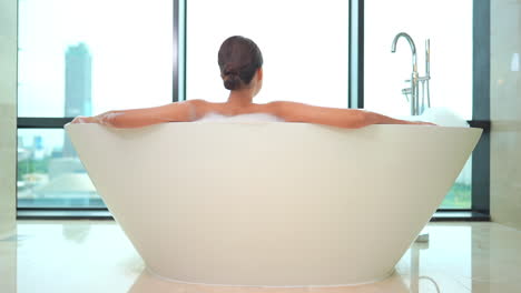 rear view of woman in luxurious bathtub enjoying city view