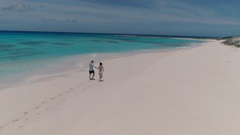 couple walking hand in hand seen from behind leaving footprints sand of deserted beach