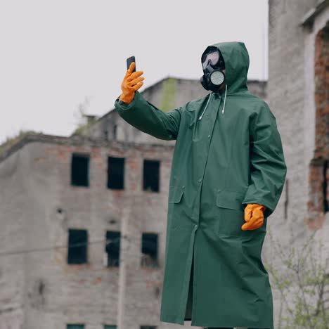 human in a protective suit and gas mask with a phone. unrecognizable person in safety uniform, gloves and respirator doing selfie in the destroyed place during radiation